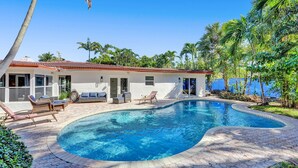 A poolside area with a house, lounge chairs, and a swimming pool.