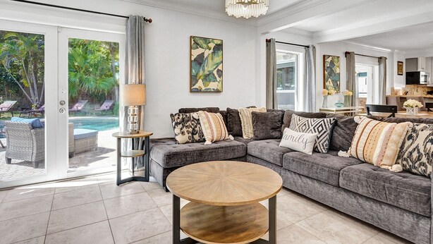 A modern living room with a grey sectional sofa, a round coffee table, and a pool view.