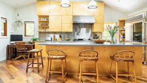 Una cocina moderna con armarios de madera, una isla central con taburetes altos, electrodomésticos de acero inoxidable e iluminación colgante.