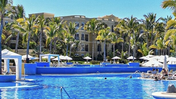 Un área de piscina con agua cristalina, rodeada de palmeras y sillones de descanso.