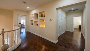 A spacious hallway with wooden flooring, a staircase with a white railing, and built-in shelves with decorative items. - Large Luxurious Estate on Golf Course w/pool/spa in Gated Community (Henderson)