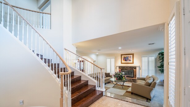 A spacious living area with a fireplace, a sofa, and a coffee table. A staircase with wooden railings leads to an upper level. - Large Luxurious Estate on Golf Course w/pool/spa in Gated Community (Henderson)