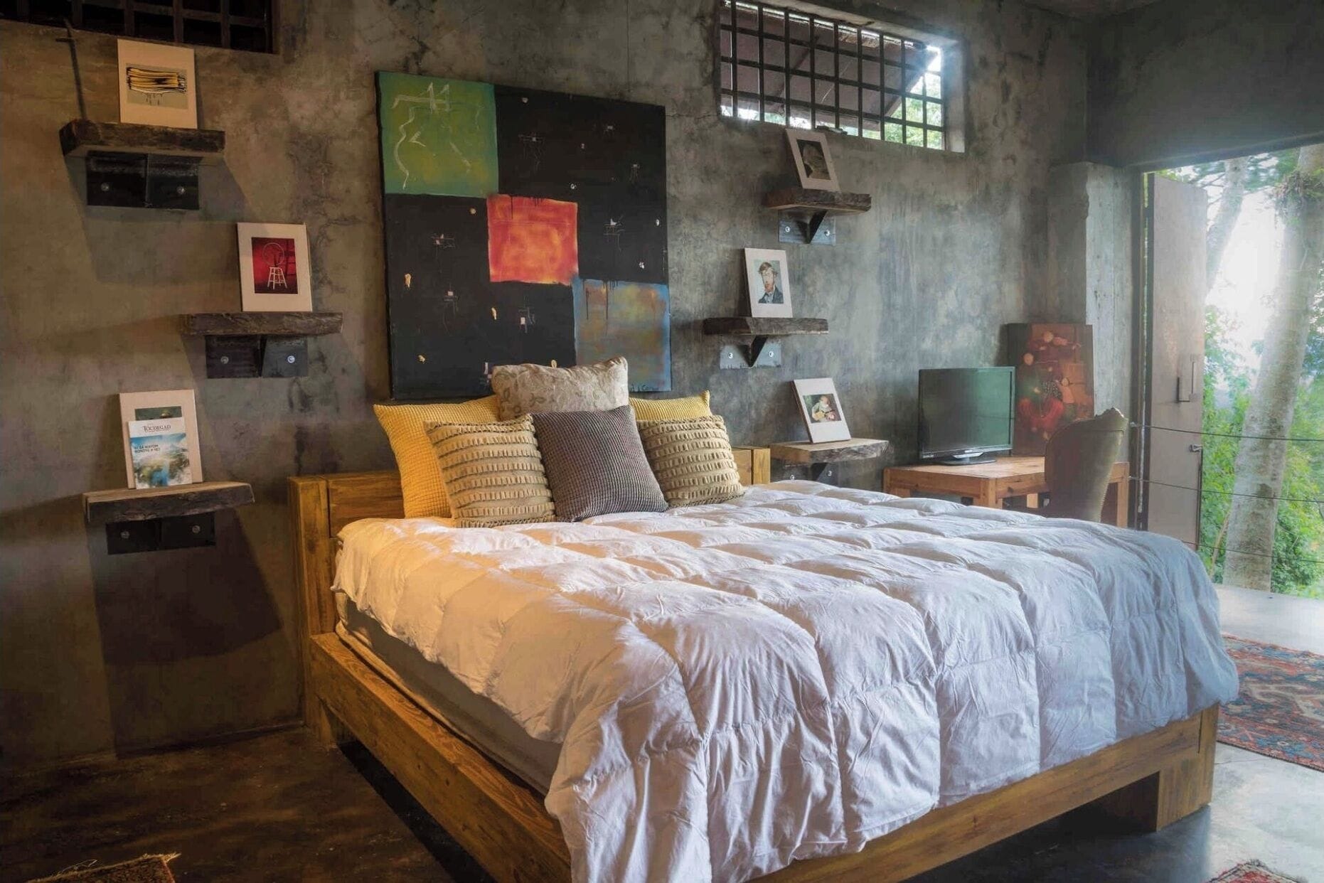 A bedroom with a wooden bed, multiple pillows, a television, and artwork on the walls.