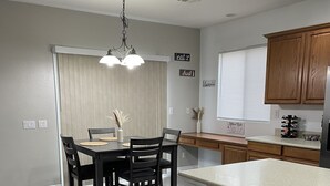 Eine moderne Küche mit Essbereich, ausgestattet mit Holzboden in heller Farbe, dunklen Holzstühlen, einer zentralen Kochinsel mit Barhocker und einer Pendelleuchte über dem Esstisch.