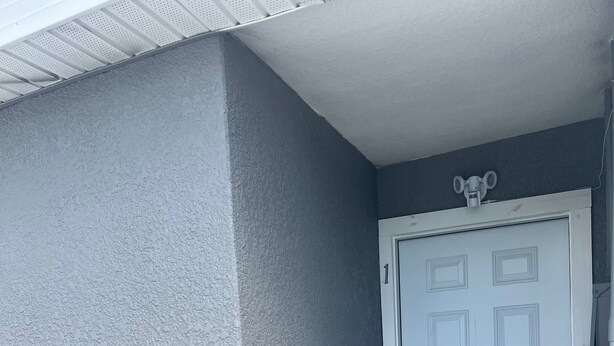Una puerta blanca con el número '1' encima, un felpudo con un diseño geométrico y una pared gris con textura.