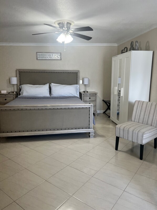 A bedroom with a bed, nightstands, a ceiling fan, a wardrobe, and a chair.