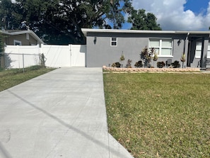 A residential house with a concrete driveway leading to a garage, surrounded by a white fence and a well-maintained lawn.