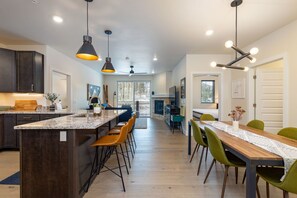 A modern kitchen with dark cabinets, a large island, and a dining area with a wooden table and green chairs.