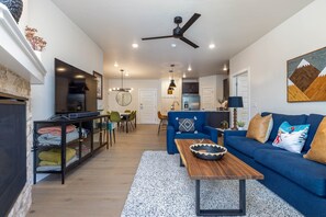 A modern living room with a blue sofa, a wooden coffee table, and a dining area with chairs and a table.
