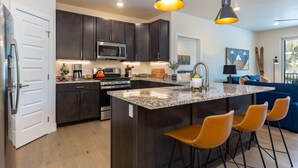 A modern kitchen with dark cabinets, stainless steel appliances, and a central island with bar stools. - Luxury Condo, Hot Tub, Balcony, Shuttle to Ski Slopes (Keystone)