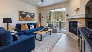 A modern living room with a blue sofa set, a wooden coffee table, and a fireplace. - Luxury Condo, Hot Tub, Balcony, Shuttle to Ski Slopes (Keystone)