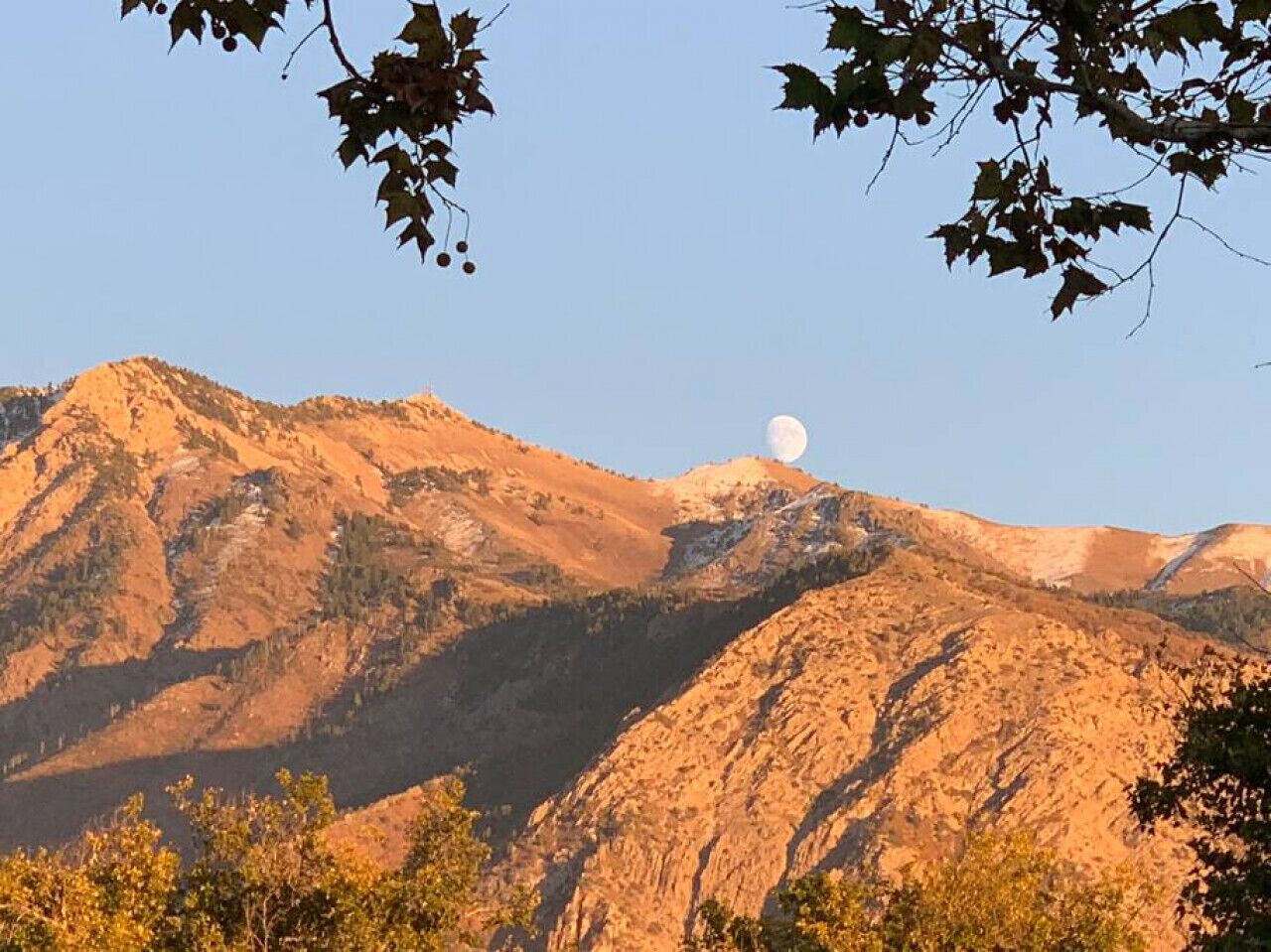 Un paysage montagneux, avec une lune bien visible dans le ciel.