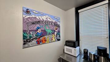 A kitchen with a wall-mounted cartoon mural, a window with blinds, and a coffee maker on the counter.