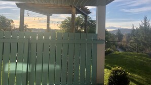 A wooden pergola with string lights, overlooking a grassy area and trees. - Olympic Views - Cozy Modern 2BR Suite (Victoria)