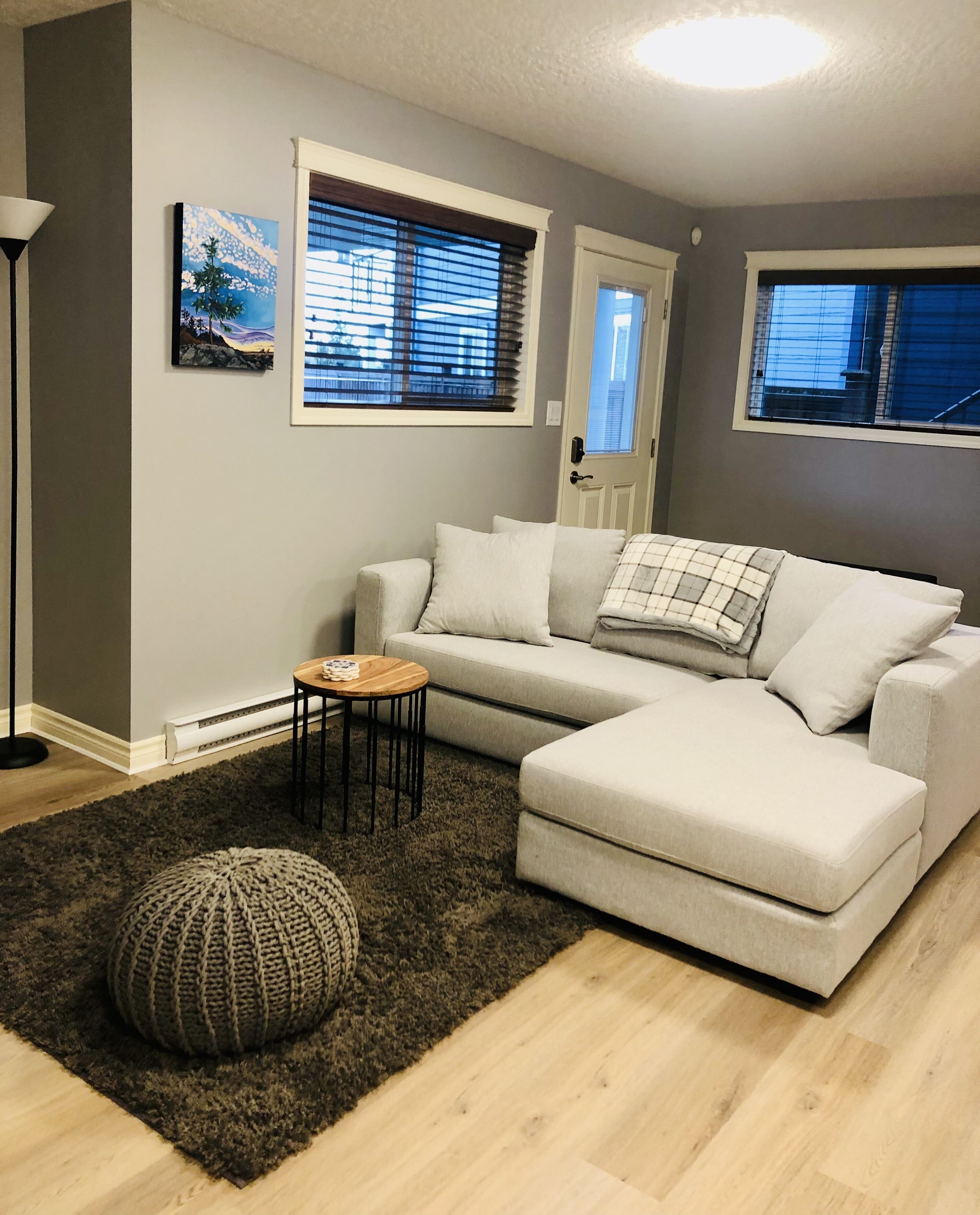 A living room with a sectional sofa, a small round table, and a knitted pouf.