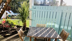 A wooden table with four chairs, a small garden with plants and a statue, and a blue fence in the background. - Olympic Views - Cozy Modern 2BR Suite (Victoria)