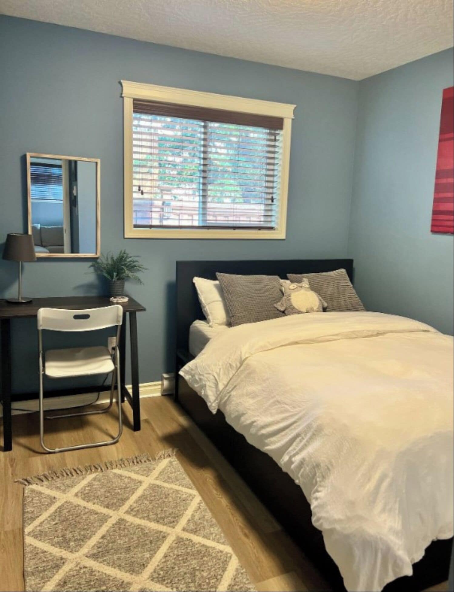 Une chambre à coucher avec un lit, un bureau avec une chaise, une fenêtre avec des stores et un tapis.