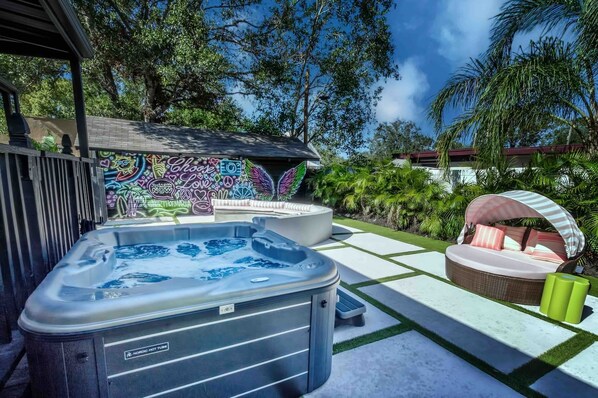 A hot tub with a Nordic logo, a mural with various symbols and text, and a covered seating area with cushions. - Retro FL Charm | Pool + Spa | AMI + Downtown | IMG (Bradenton)