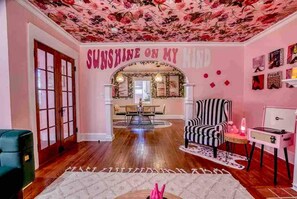 A room with a floral ceiling, a sign reading 'SUNSHINE ON MY KIND,' a striped armchair, a small table with a record player, and a patterned rug. - Retro FL Charm | Pool + Spa | AMI + Downtown | IMG (Bradenton)