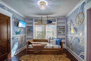 A bedroom with a bed, shelves, a television, and a ceiling fan. - Retro FL Charm | Pool + Spa | AMI + Downtown | IMG (Bradenton)