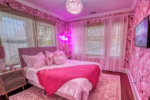 A bedroom with a bed, bedside table, and a neon sign.