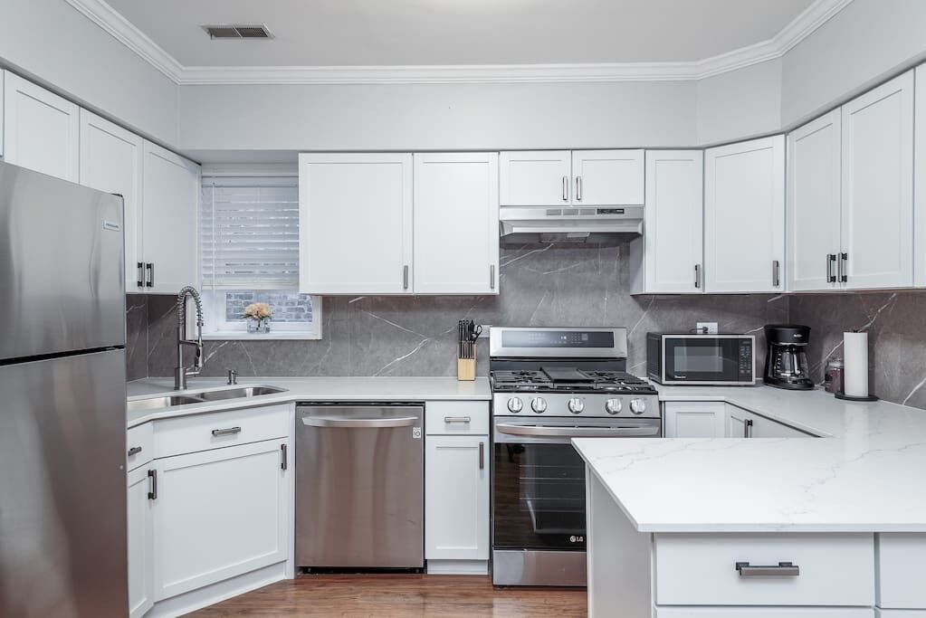 A modern kitchen with white cabinets, stainless steel appliances, and a marble countertop.
