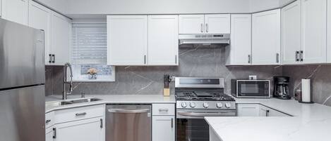 A modern kitchen with white cabinets, stainless steel appliances, and a marble countertop.