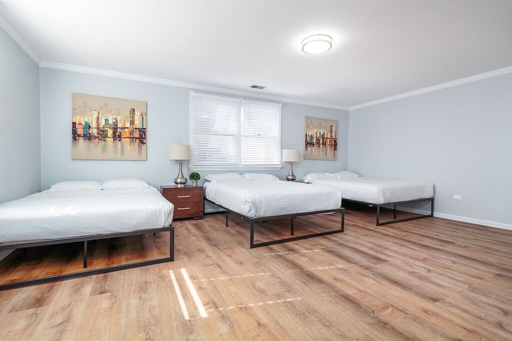A bedroom with three single beds, a window with blinds, and two wall-mounted lamps.