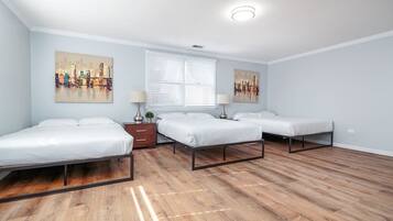 A bedroom with three single beds, a window with blinds, and two wall-mounted lamps.