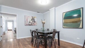 A dining area with a dark wooden table and chairs, a vase with dried flowers, and two abstract paintings on the walls. - Beautiful, Remodeled Penthouse Unit in Old Town! (Chicago)