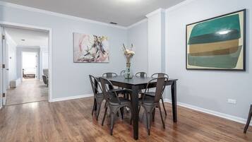 A dining area with a dark wooden table and chairs, a vase with dried flowers, and two abstract paintings on the walls.