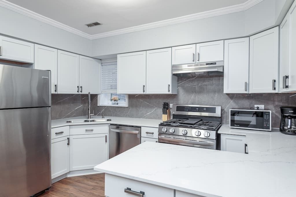 Una cocina moderna con armarios blancos, electrodomésticos de acero inoxidable y encimera de mármol.
