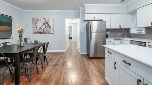 A modern kitchen with white cabinets, stainless steel appliances, and a dining area with a dark table and chairs. - Beautiful, Remodeled Penthouse Unit in Old Town! (Chicago)