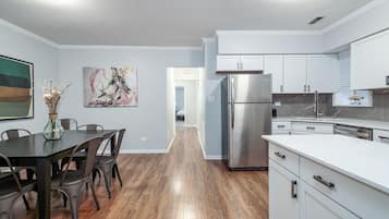A modern kitchen with white cabinets, stainless steel appliances, and a dining area with a dark table and chairs.