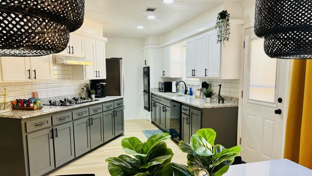 Una cocina moderna con armarios grises, encimera blanca y un comedor con mesa blanca y plantas verdes.