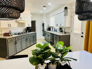 A modern kitchen with grey cabinets, a white countertop, and a dining area with a white table and green plants.