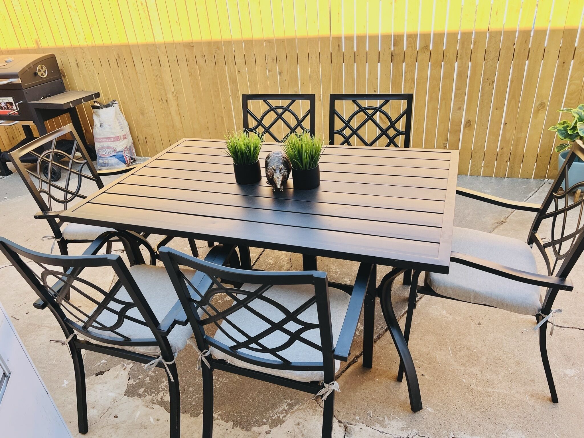 A patio with a table and chairs, a grill, and a wooden fence.