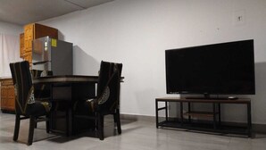 Een eethoek met een tafel en stoelen, een televisie op een standaard en een koelkast.