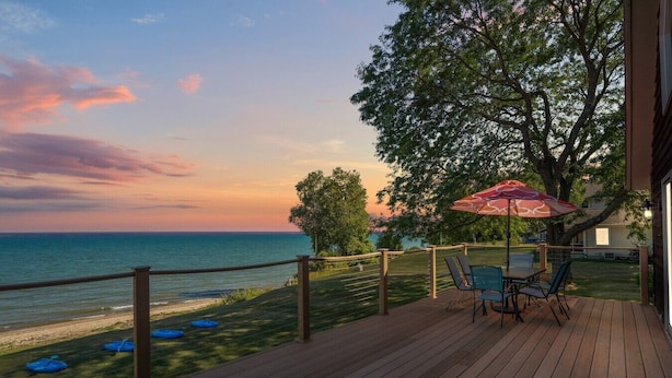 Een houten terras met een tafel en stoelen, met uitzicht op een waterpartij en een zonsondergang.