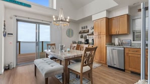 Een moderne keuken met houten kastjes, een eethoek met een marmeren tafel, en uitzicht op de oceaan door een schuifdeur van glas.