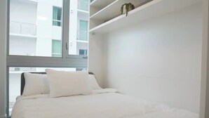 A modern bedroom with a large bed, white walls, and a view of a building outside. - Lovely studio unit in Miami-Van Dennis (Miami)