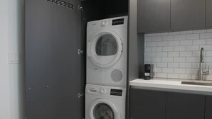 A laundry room with two stacked front-loading washing machines, a modern sink, and a tiled backsplash. - Lovely studio unit in Miami-Van Dennis (Miami)