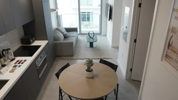 A modern kitchen with a dining area, a sofa, and a small table with a plant. - Lovely studio unit in Miami-Van Dennis (Miami)