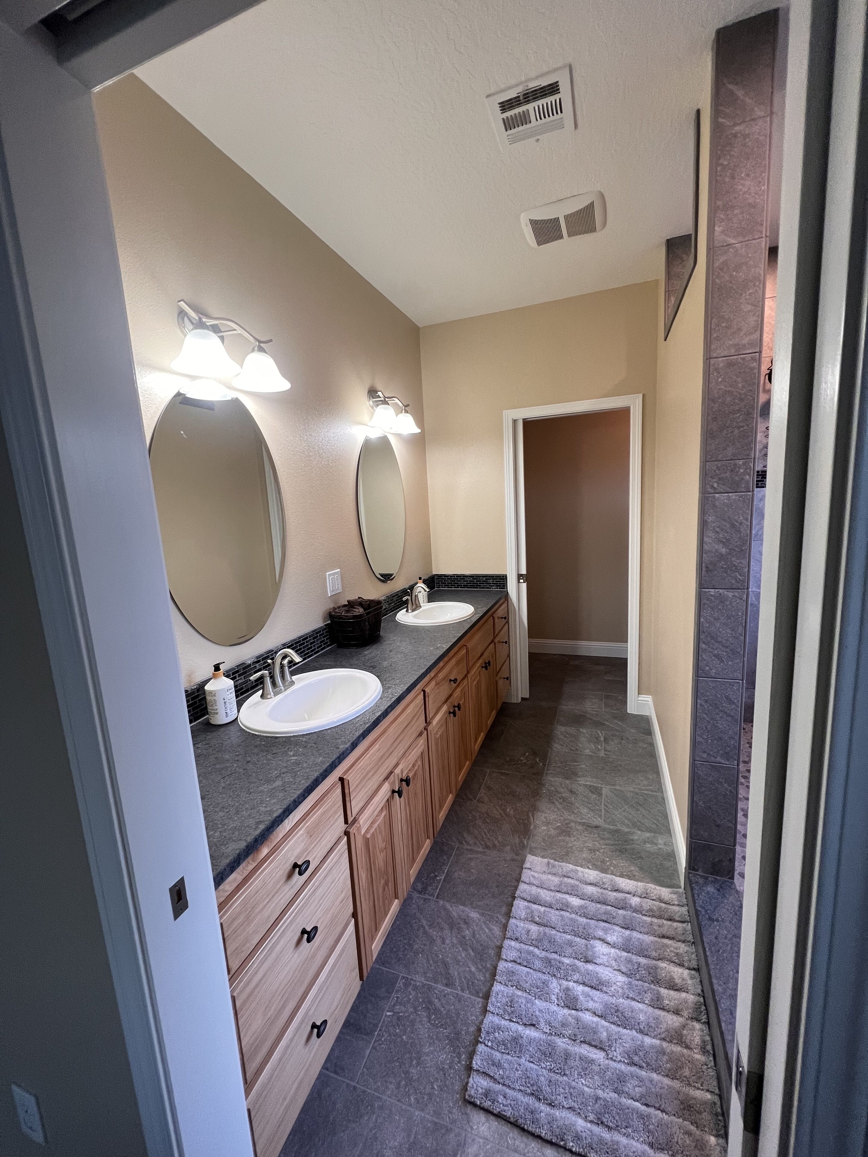 A modern bathroom with two sinks, a large mirror, and a walk-in shower.