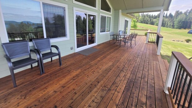 Une terrasse couverte avec un plancher en bois, de grandes fenêtres et une table avec des chaises.