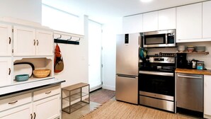 Une cuisine moderne avec des meubles blancs, des appareils en acier inoxydable et une petite table en bois.