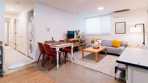 Un espace de vie compact comprenant un coin repas, un canapé, une table basse et un téléviseur. Il y a également un lave-linge et un petit coin cuisine.