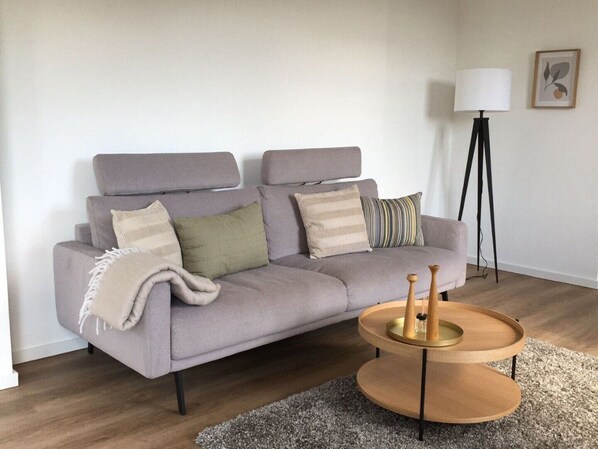 A modern living room with a grey sofa, a round wooden coffee table, and a floor lamp. - Quiet vacation home in a rural setting with a garden in the Münsterland region (Gescher)