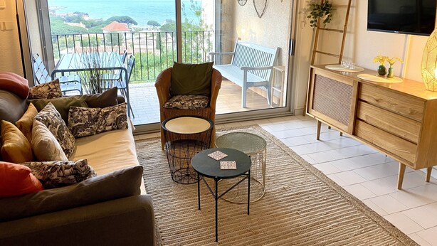 Ein Wohnzimmer mit einer Couch, einem runden Tisch, einem Fernseher und einem Balkon mit Meerblick.