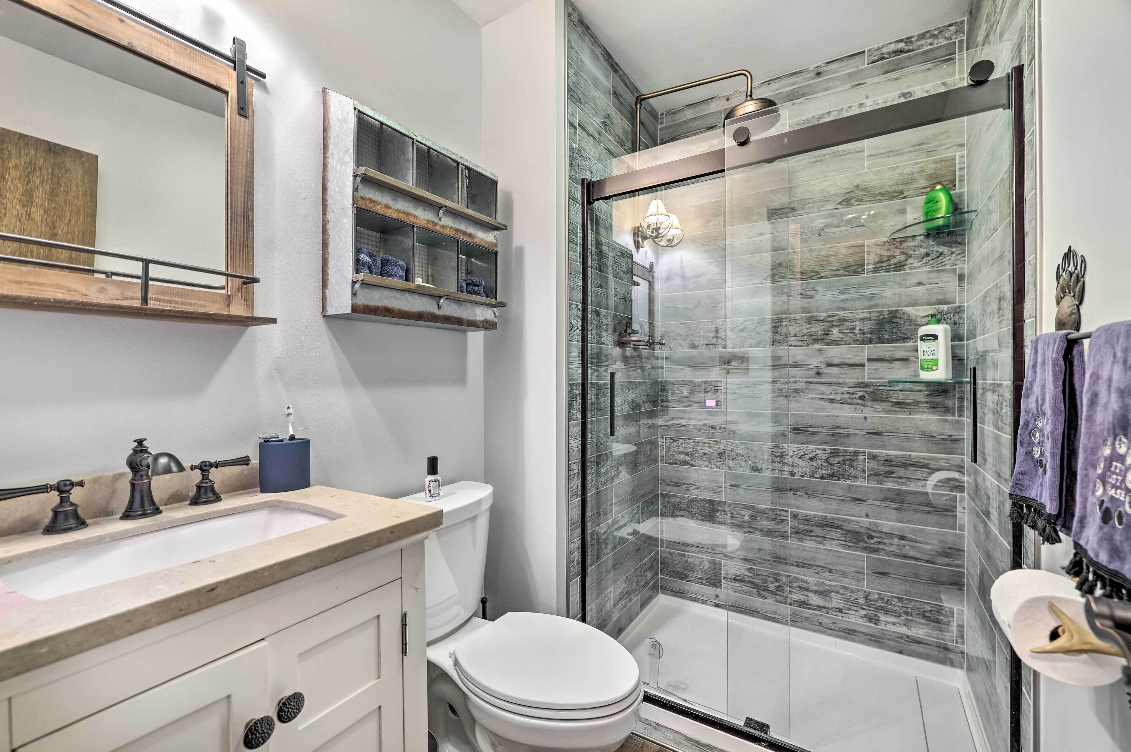 Un baño moderno con ducha envuelta en vidrio, tocador con lavamanos y un inodoro.